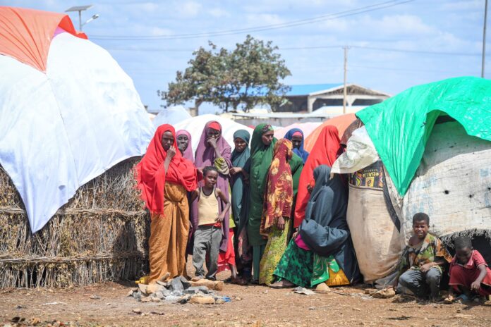 Women and children stand outside their makeshift shelters within Raama Cadeey Internally Displaced Persons camp in Baidoa, Somalia.