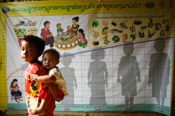 A young Laotian boy carries a child on his back outside the Farmer Nutrition School (FNS) in Houayjay village of La District, Lao People's Democratic Republic.